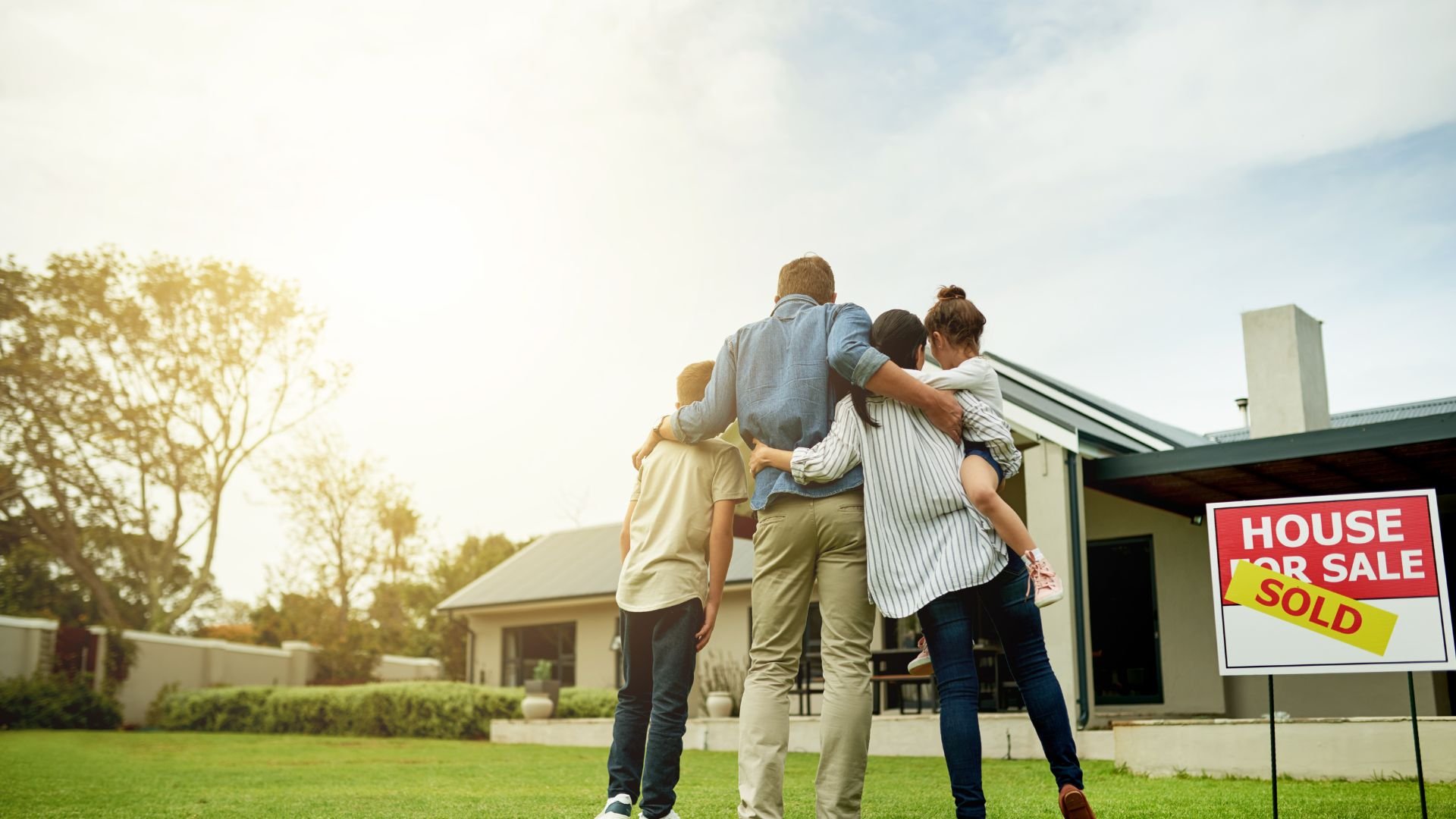 Family standing together in front of new home with sold sign