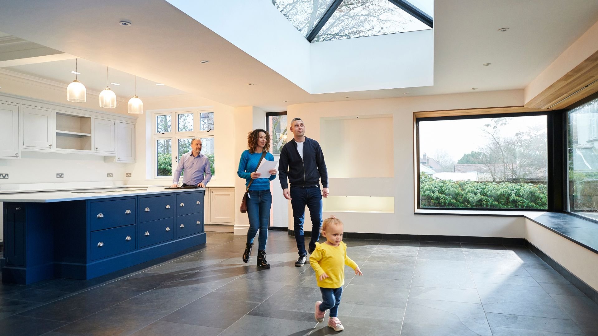 Family viewing modern kitchen with child running in foreground
