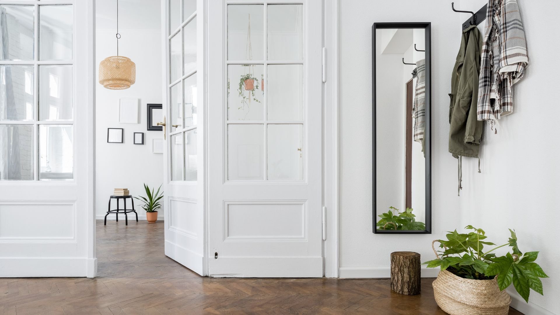 Bright entryway with white doors, plants, woven lamp, and hanging jackets